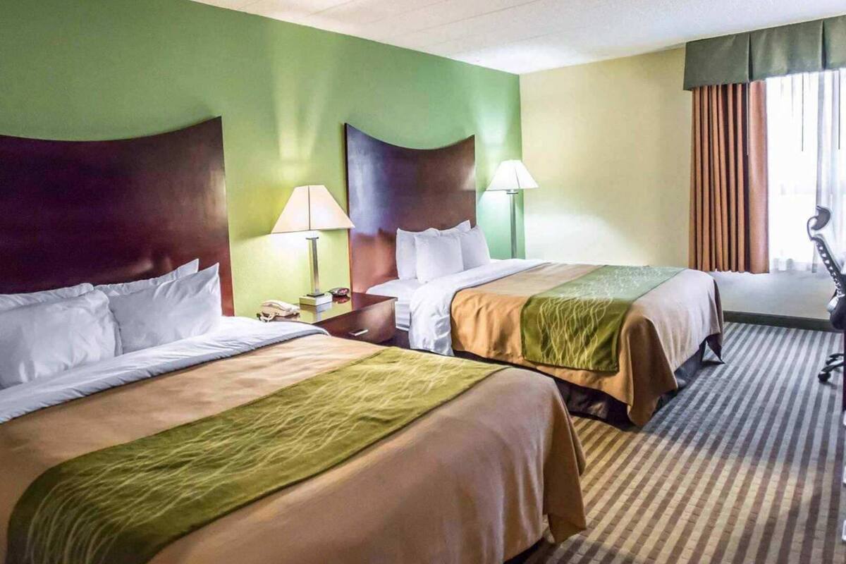 A hotel room with two beds, a nightstand, a lamp, a telephone, and a window with curtains.