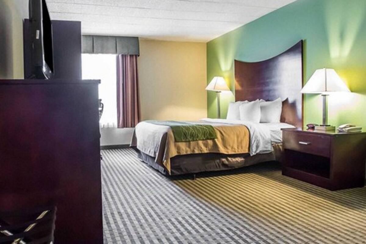 A hotel room with a bed, two bedside lamps, a TV, and a desk with a phone.