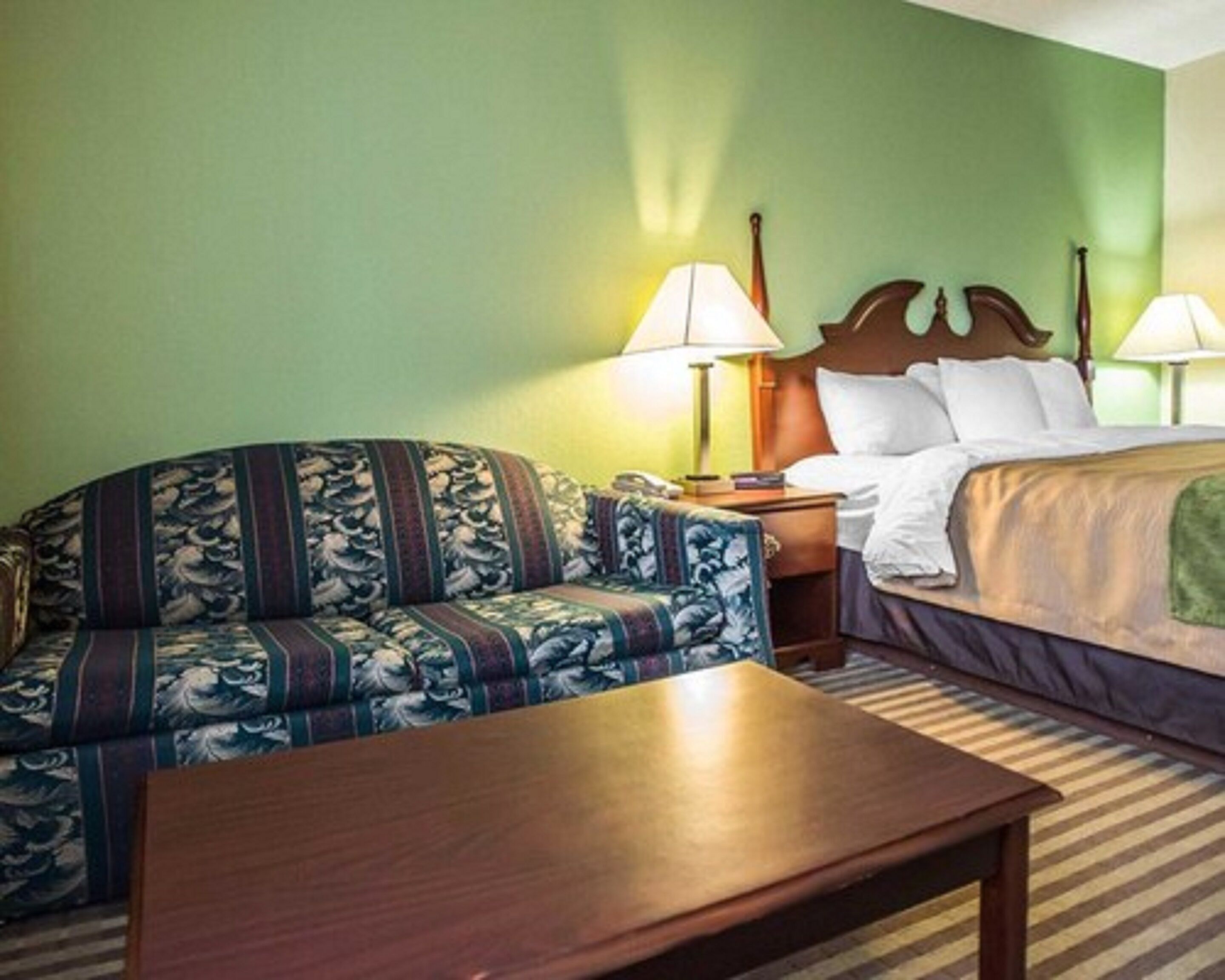 A hotel room with a sofa, a bed, a nightstand, and two lamps.