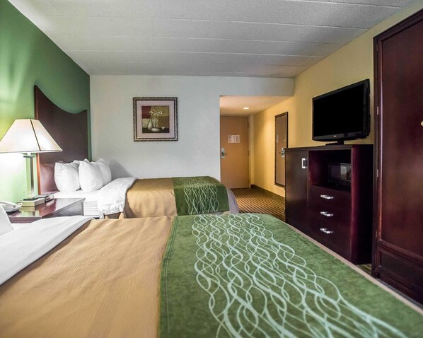 A hotel room with a bed, a desk with a lamp, a television on a cabinet, and a framed picture on the wall.