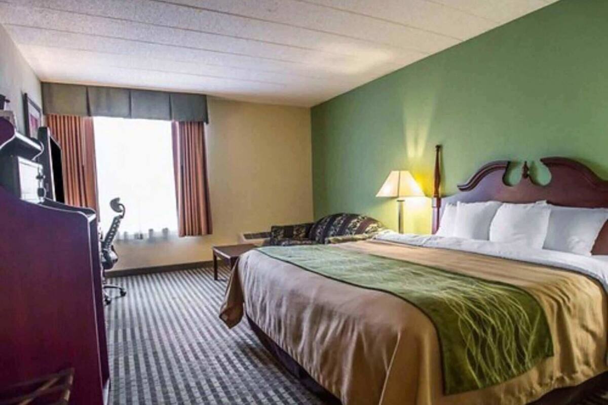 A hotel room with a bed, a desk, a lamp, and a window with curtains.
