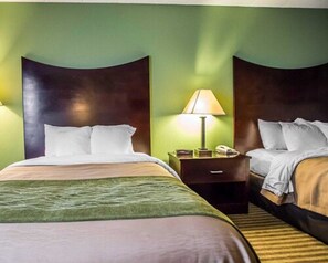 A hotel room with two beds, a nightstand with a lamp, and a green wall.