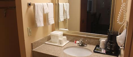 A hotel bathroom with a sink, a mirror, a hairdryer, and a coffee maker.