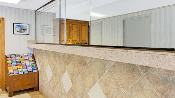 A reception area with a marble-tiled wall, a wooden cabinet, and a display of brochures. - Super 8 by Wyndham Laurel (Laurel)