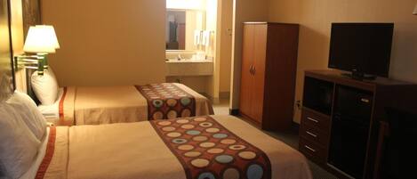 A hotel room with two beds, a television, a wardrobe, and a bathroom visible through an open door.