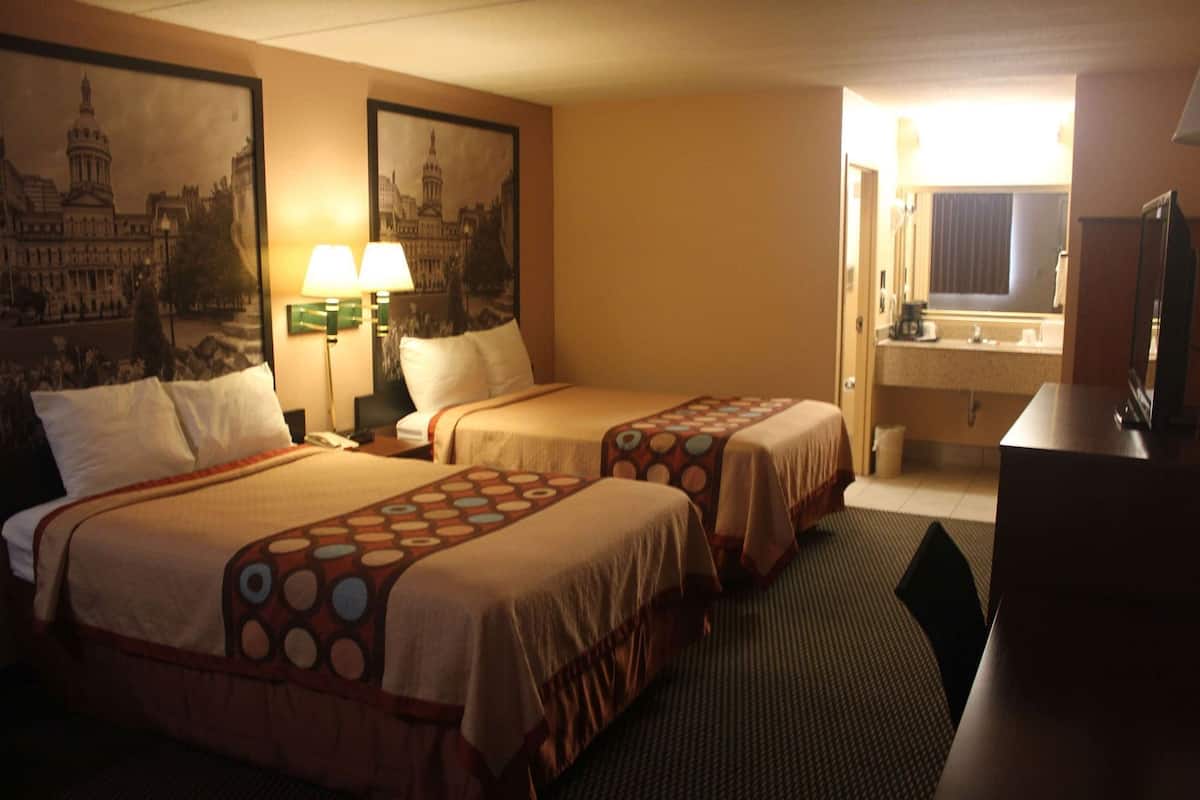 Ein Hotelzimmer mit zwei Betten, einem Schreibtisch, einem Fernseher und einem durch eine offene Tür einsehbarer Badezimmer.