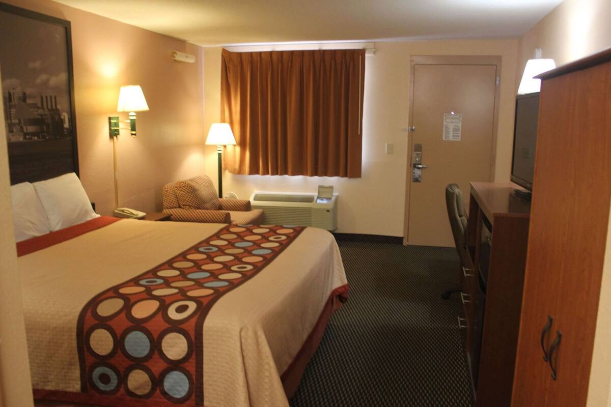 Ein Hotelzimmer mit einem großen Bett, einem Schreibtisch mit Lampe, einem Sessel, einem Fernseher und einer Tür.