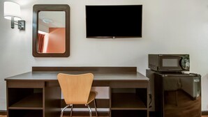 Ein Hotelzimmer mit Schreibtisch, Stuhl, Flachbildfernseher, Mikrowelle und Lampe.