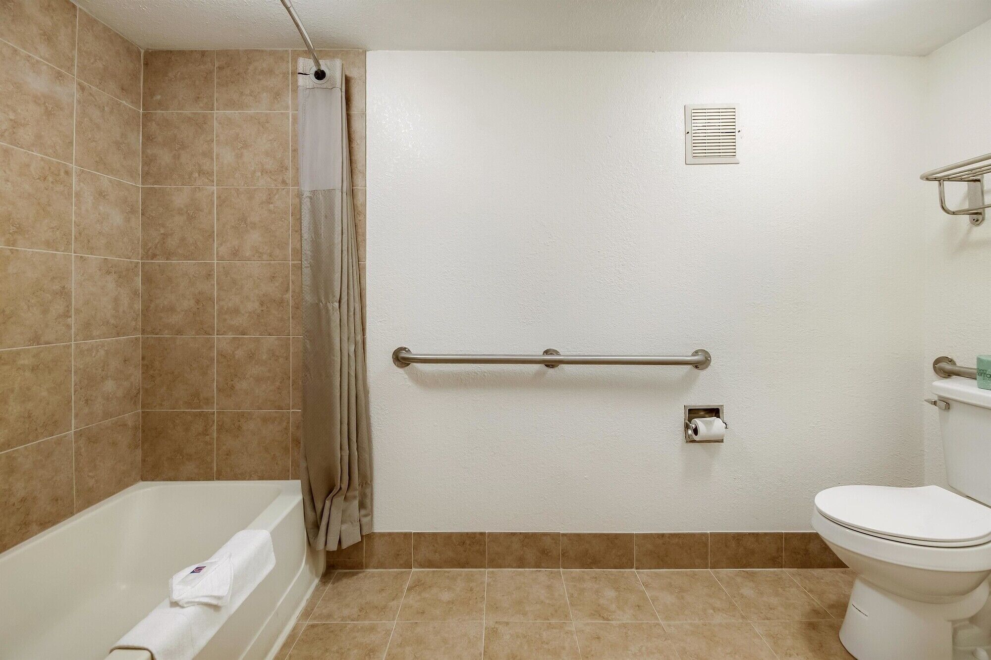 A bathroom with a bathtub, toilet, and a handrail.