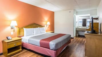A hotel room with a bed, bedside lamps, a desk with a lamp, a mirror, and a wooden floor.