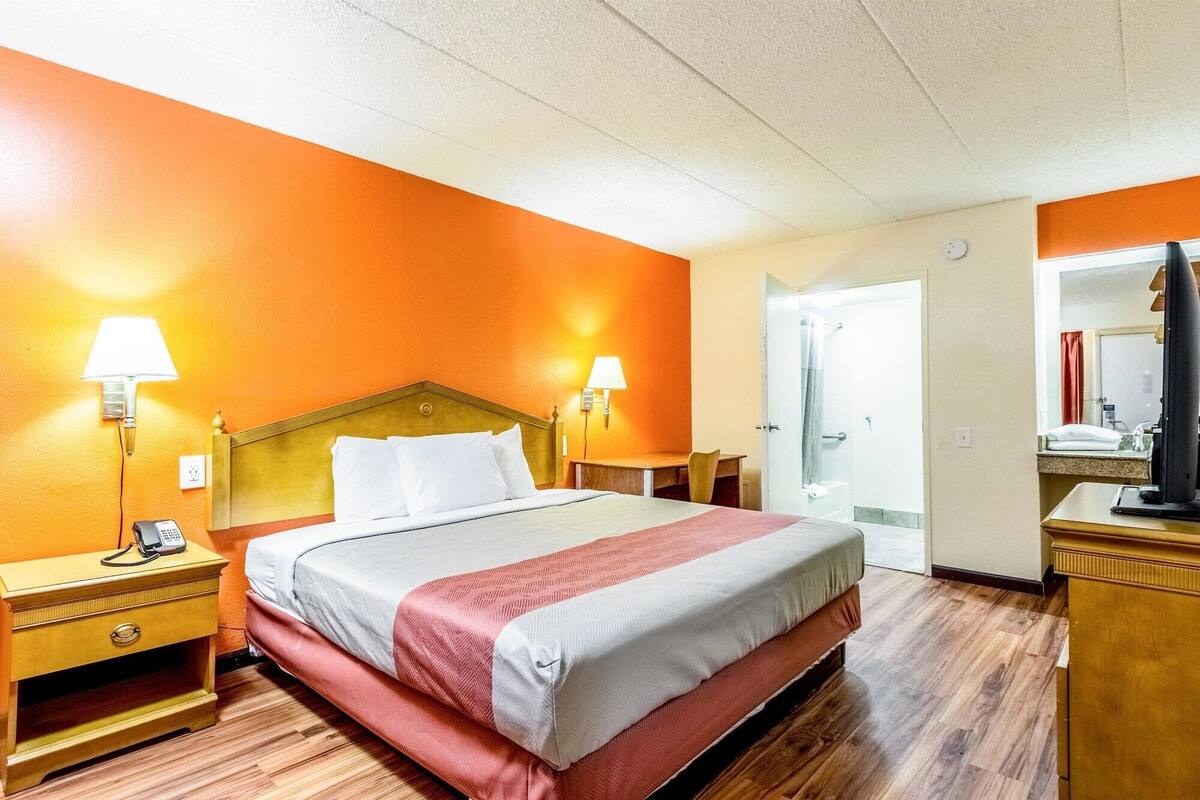 A hotel room with a bed, two bedside lamps, a telephone, a wooden nightstand, a wooden dresser, and a mirror.