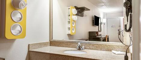 A bathroom with a granite countertop sink, a mirror, and a hairdryer on the wall.