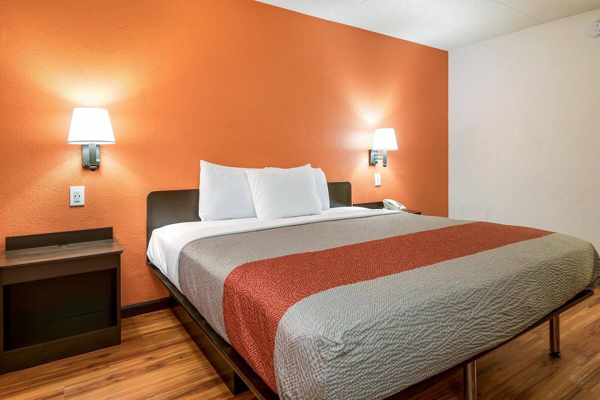 A hotel room with a bed, two bedside lamps, a nightstand, and a wooden floor.