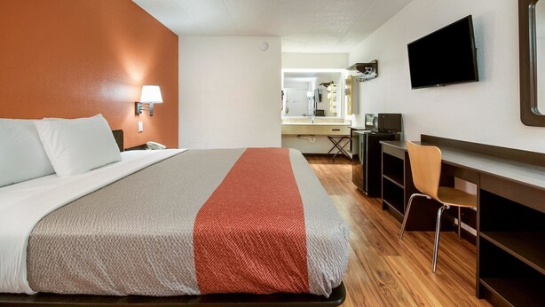 Ein Hotelzimmer mit Bett, Schreibtisch, Stuhl, Fernseher und einem im Hintergrund sichtbaren Badezimmer.