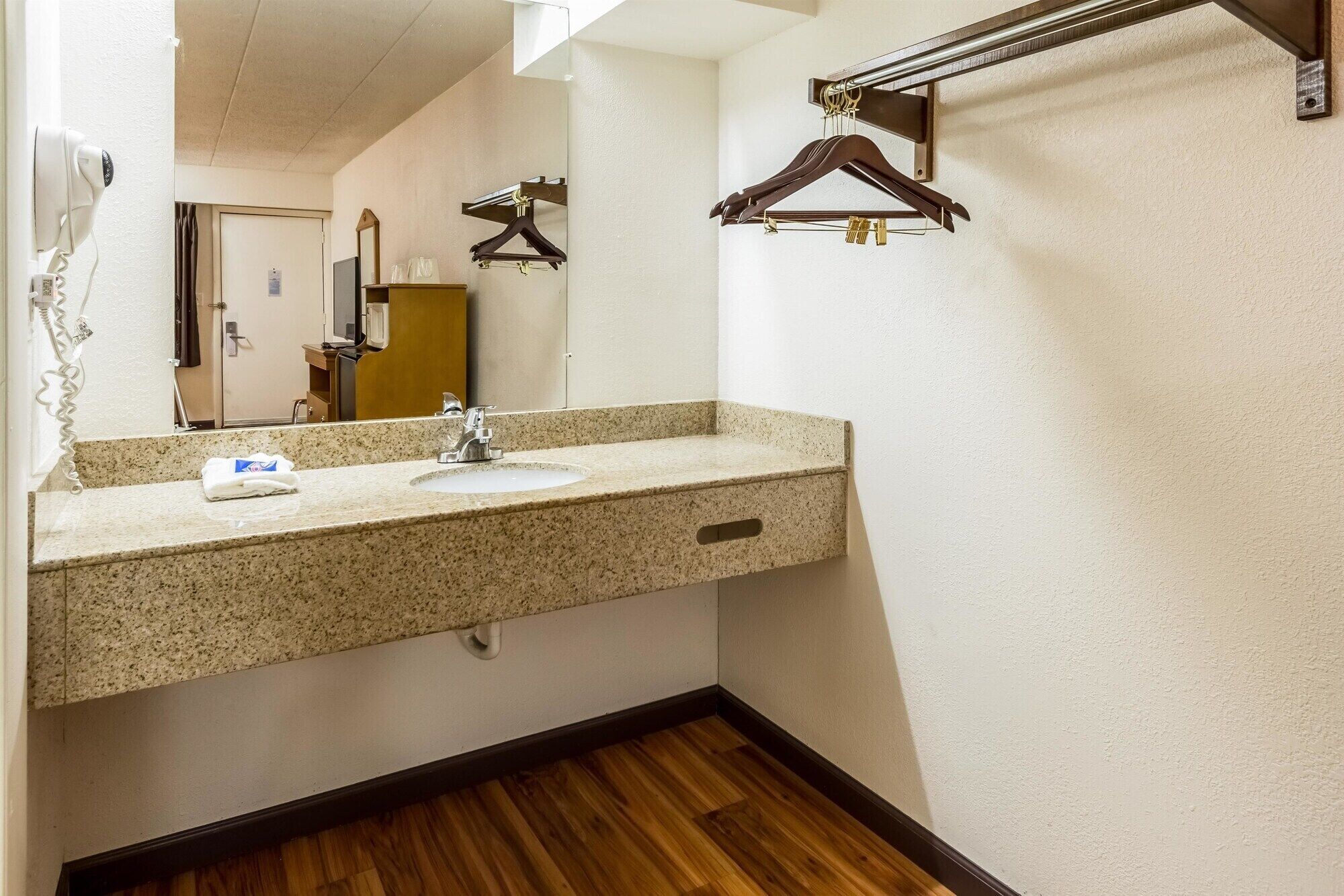 A hotel bathroom with a granite countertop sink, a mirror, a hairdryer, and a wooden hanger.