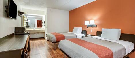 Habitación de hotel con dos camas, un escritorio, un televisor, un espejo y un baño visible a través de una puerta abierta.