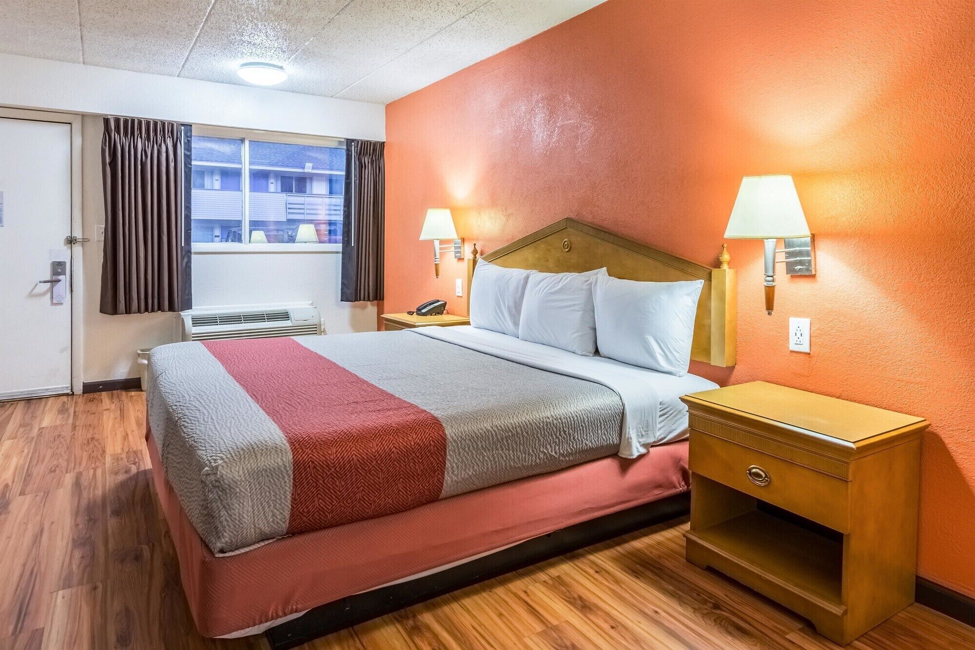 A hotel room with a bed, two bedside lamps, a nightstand, and a window with curtains.