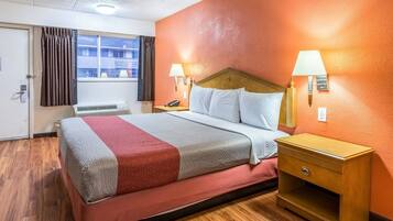 A hotel room with a bed, two bedside lamps, a nightstand, and a window with curtains.