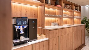 A wooden reception desk with a coffee machine, shelves with glassware, and a plant.