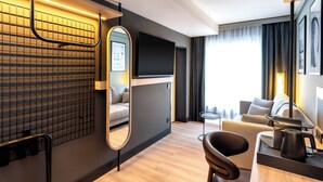 A modern hotel room with a sofa, a coffee table, a TV, and a mirror.