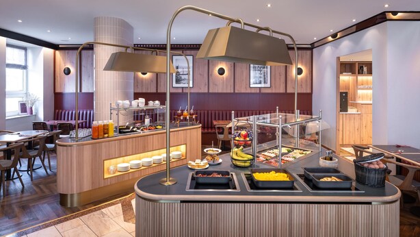A breakfast bar with various food options, a seating area with tables and chairs, and a counter with a display of breakfast items.