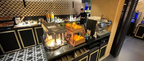 A modern breakfast bar with a patterned backsplash, a coffee machine, and a fruit display.