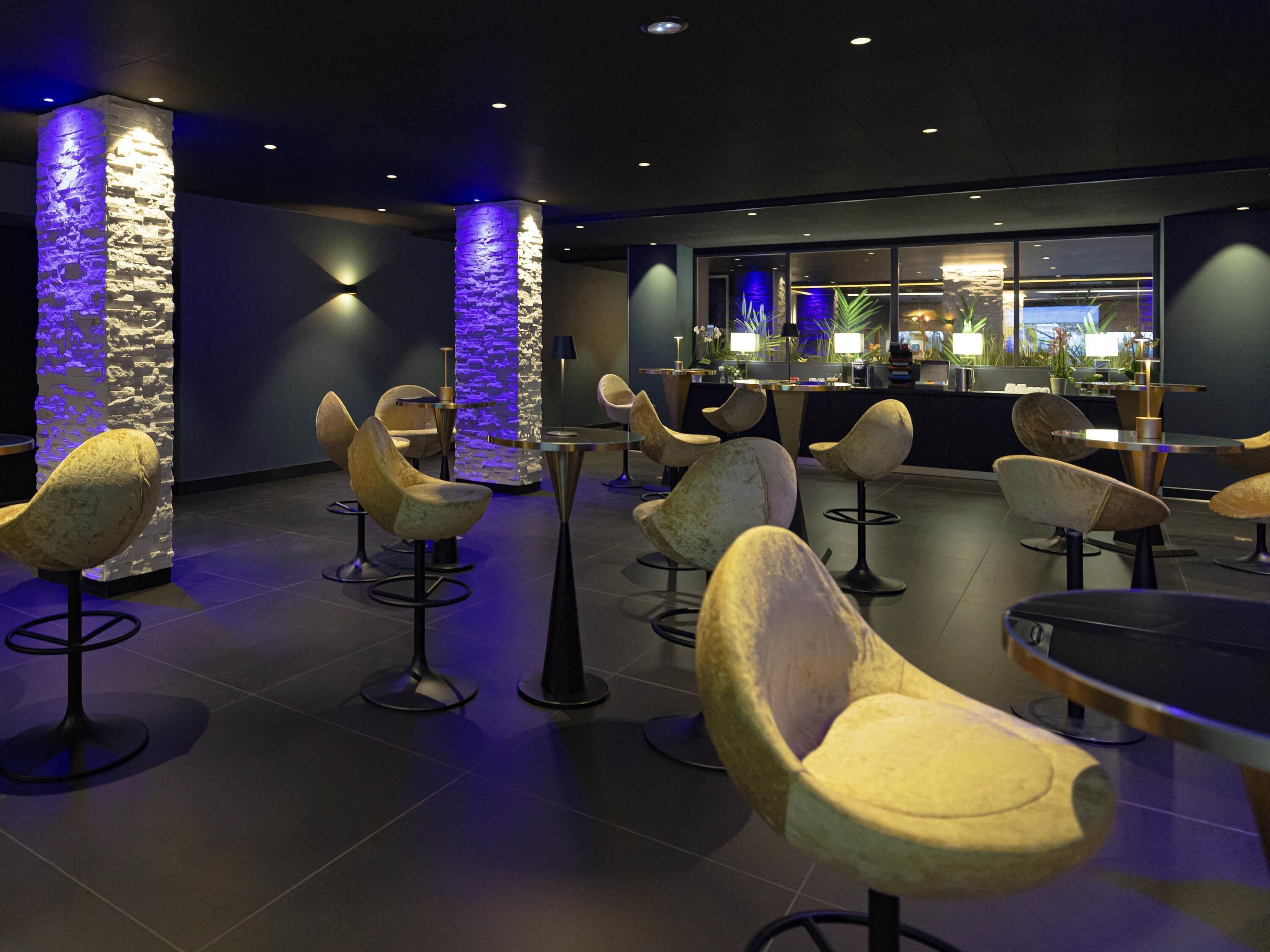 Un área de estar moderna con sillas contemporáneas y un bar al fondo.