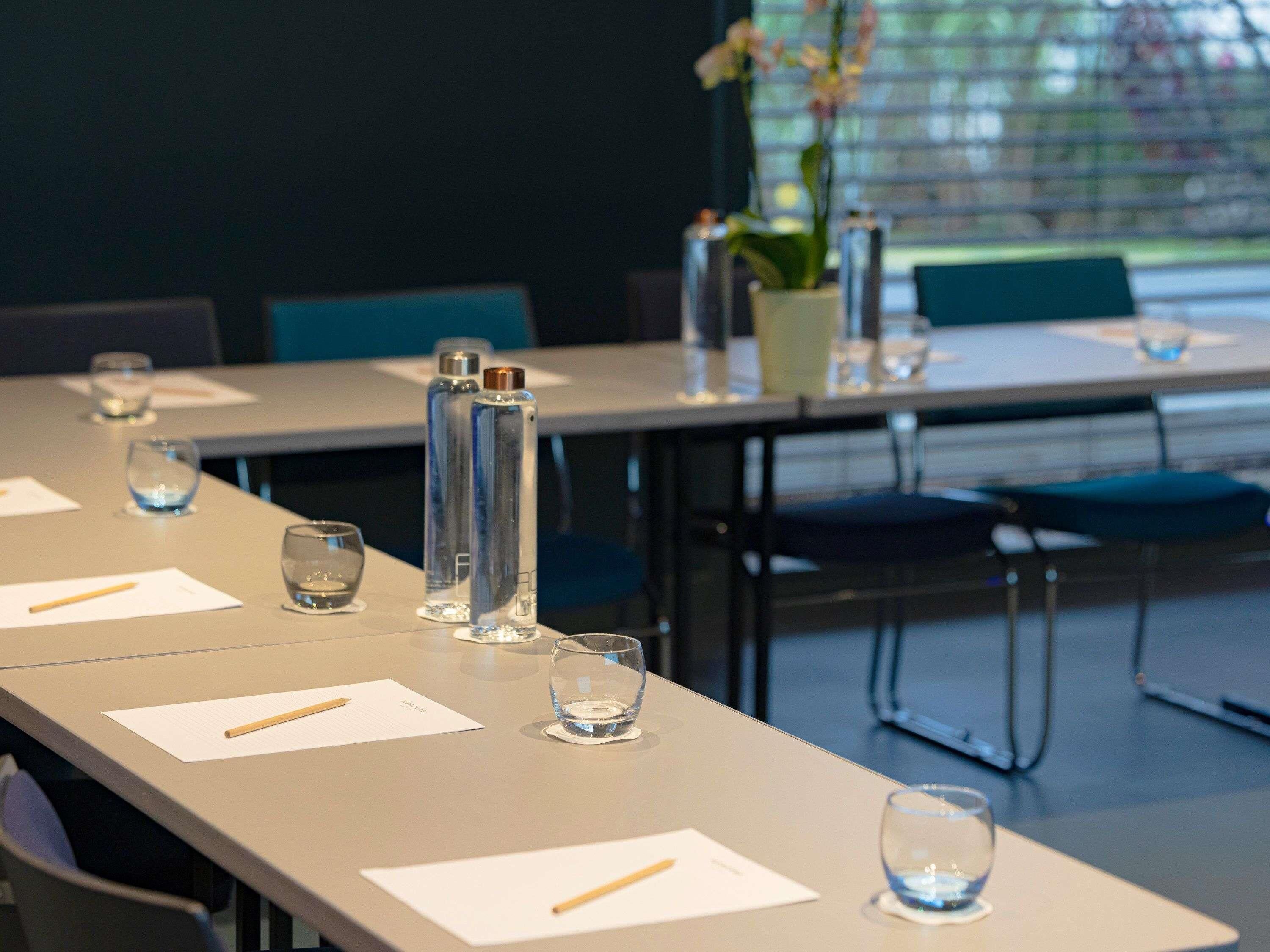 Une salle de conférence avec une longue table, des chaises et des bouteilles d’eau.