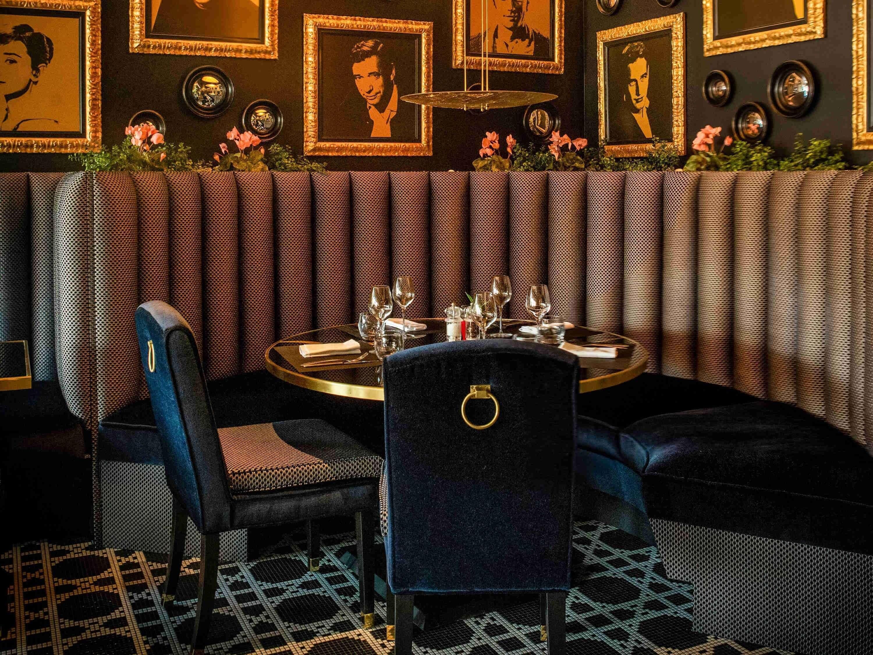 Un restaurante con mesas en cabinas, una mesa redonda con detalles dorados y retratos enmarcados en la pared.
