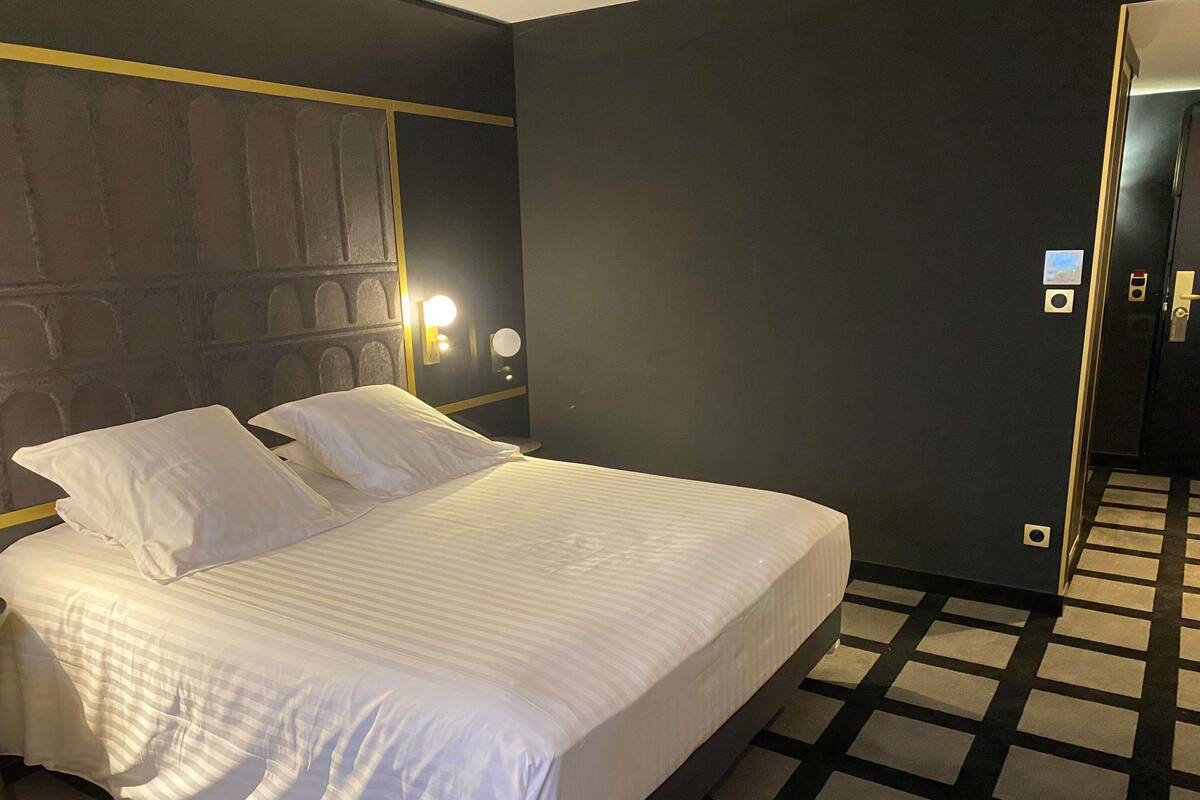 A hotel room with a large bed, two bedside tables, and a headboard with built-in lighting.