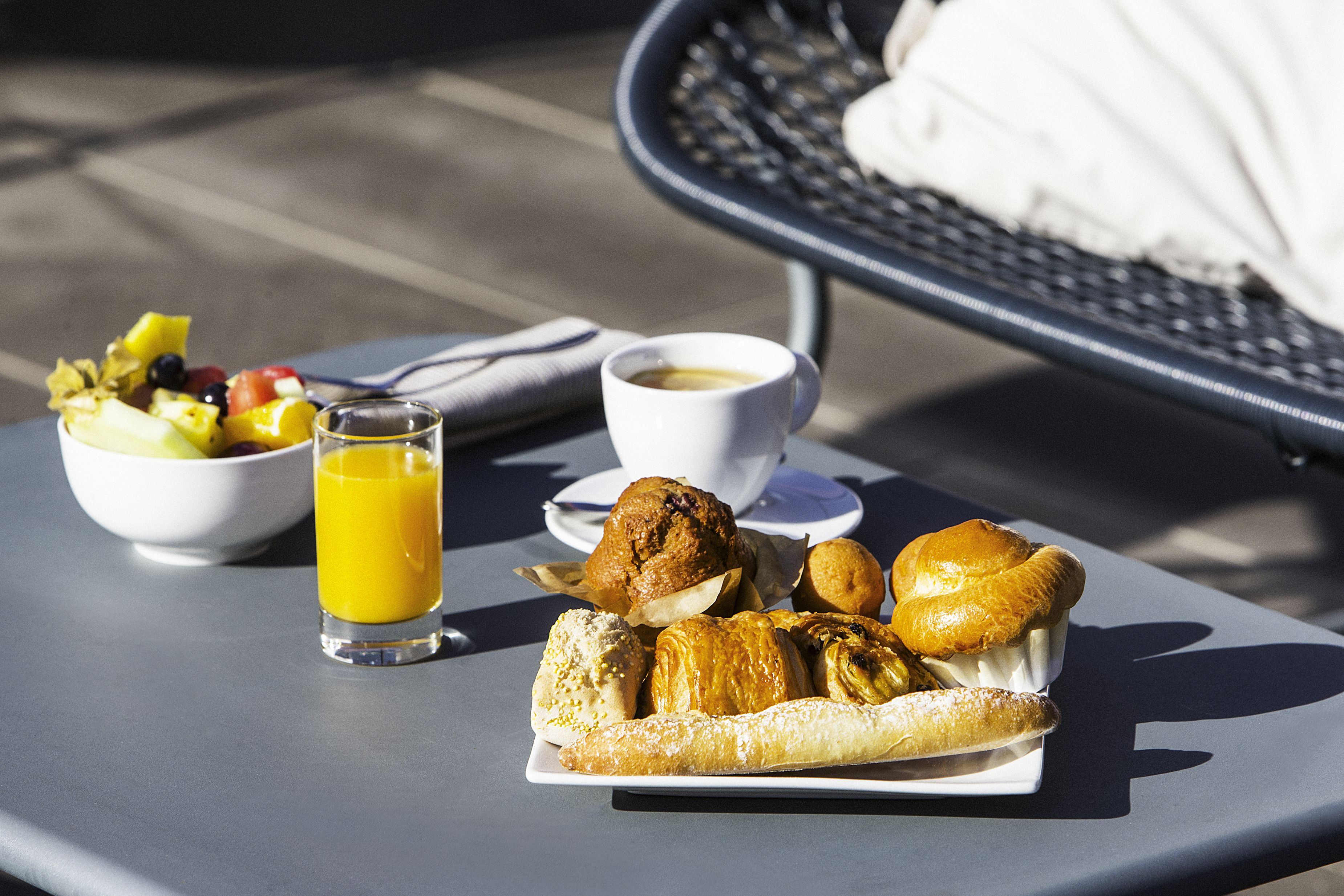 A breakfast setting with a plate of pastries, a bowl of fruit, a glass of orange juice, and a cup of coffee on a table.