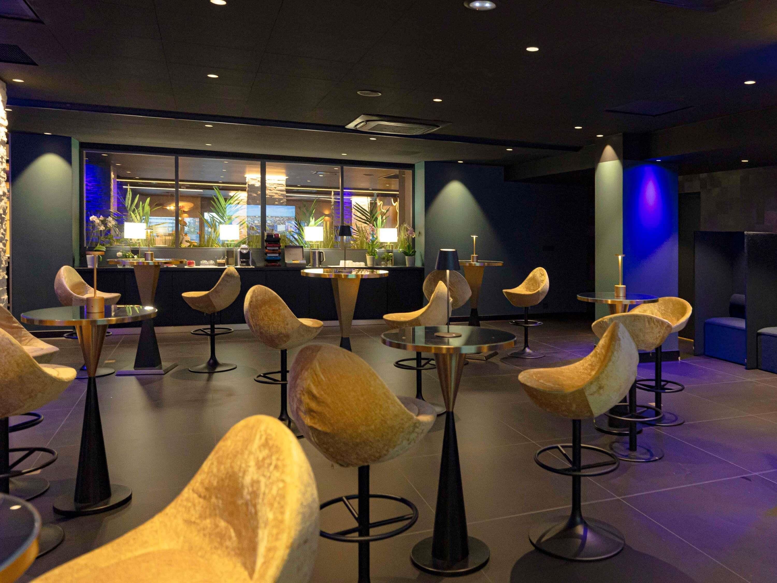 Een moderne barruimte met bijzondere stoelen, een toonbank en uitzicht op de stad.