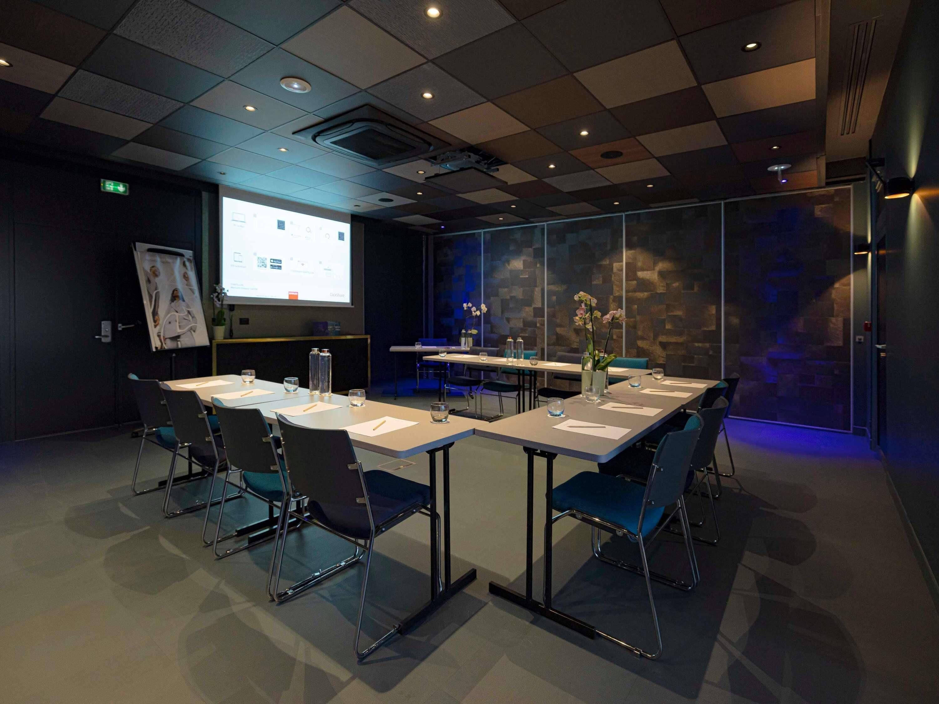 Une salle de conférence équipée d’un grand écran, de tables, de chaises et d’un mur décoratif.