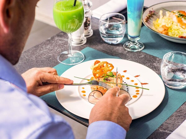 A person dining at a table with a plate of food, a glass of green drink, and a glass of water.