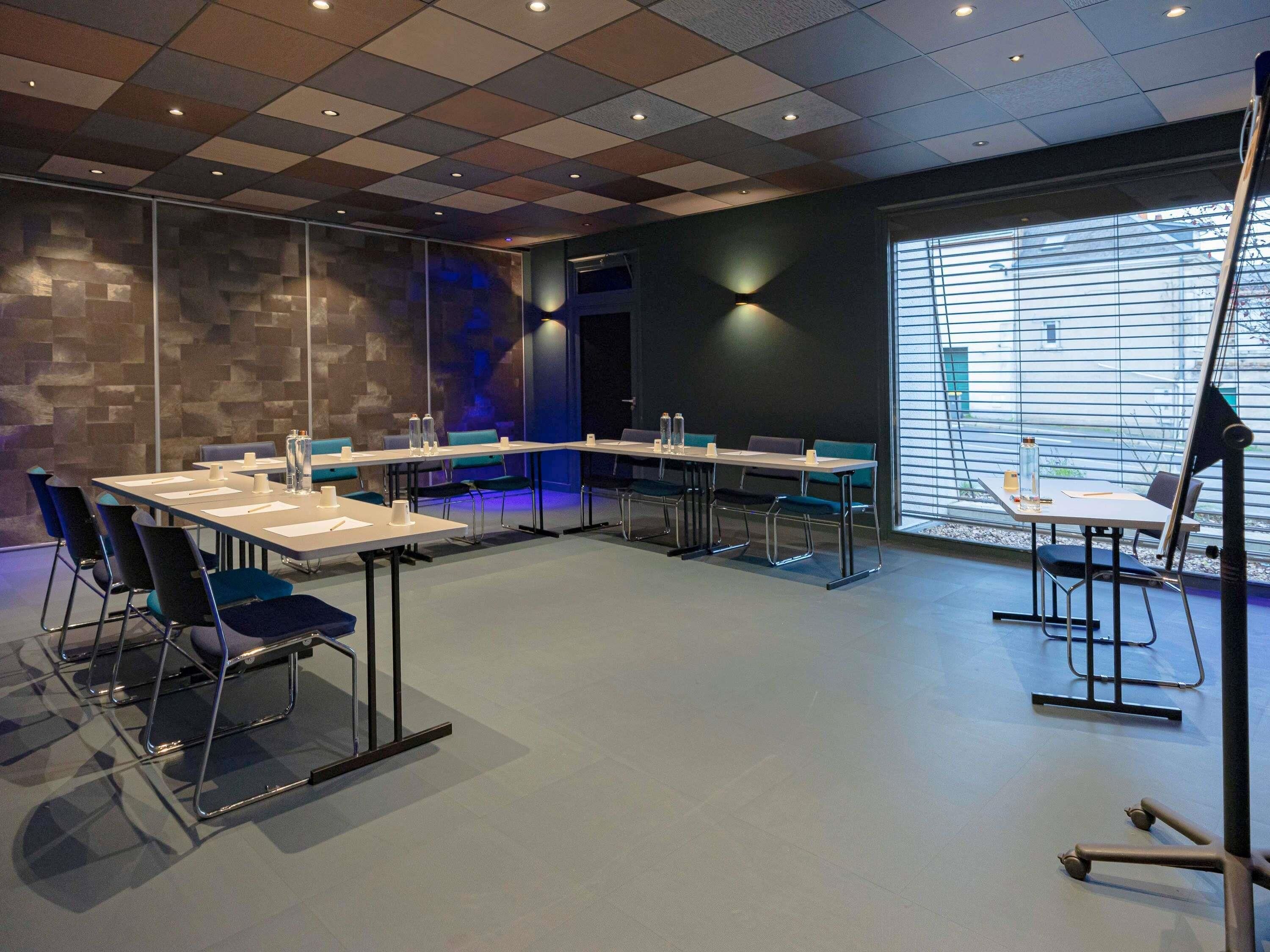 A conference room with a modern design, featuring a large table, chairs, and a projector stand.