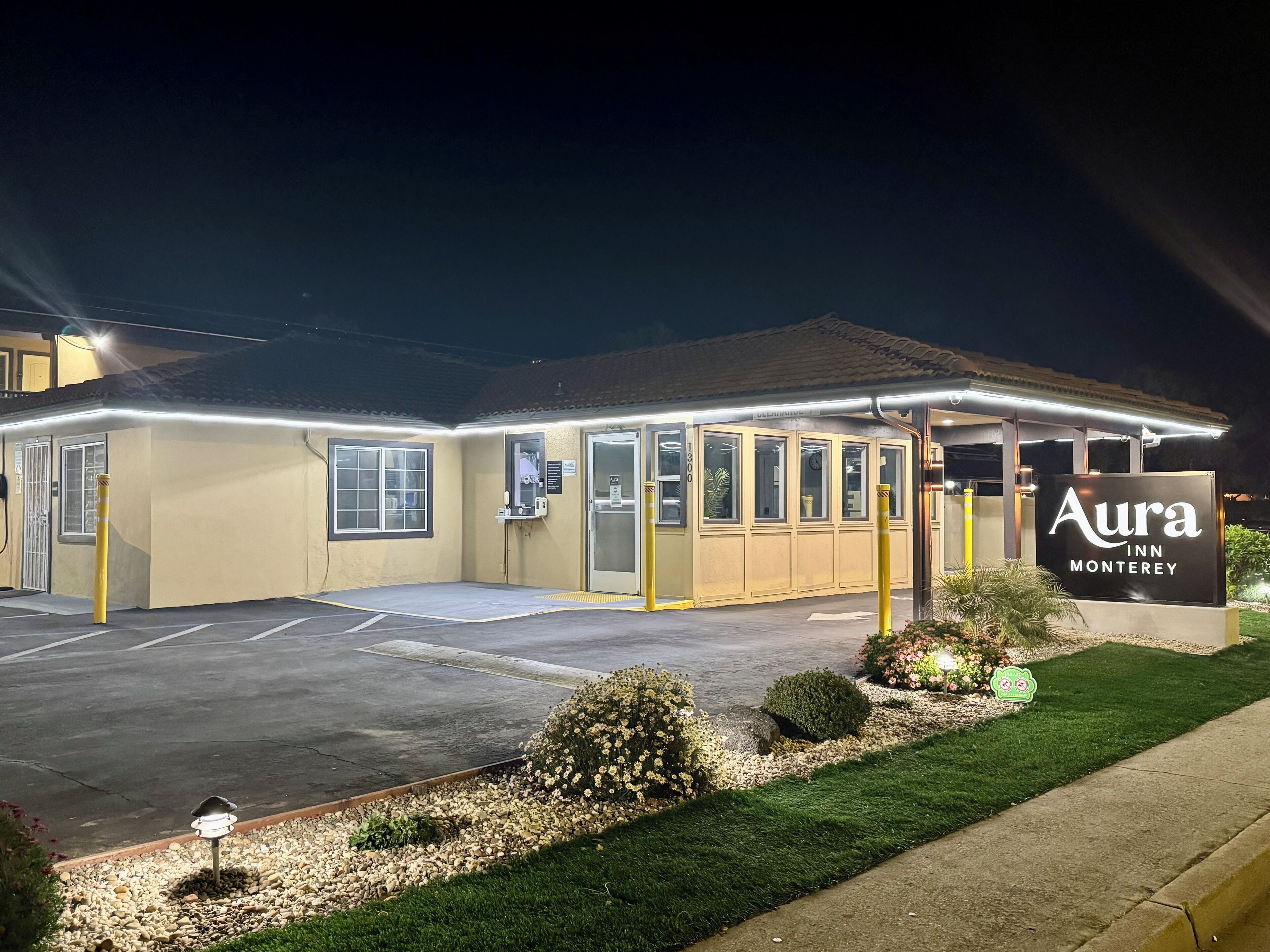 A hotel with a sign reading "Aura Inn Monterey." It features a parking lot, a covered entrance, and a well-lit facade.
