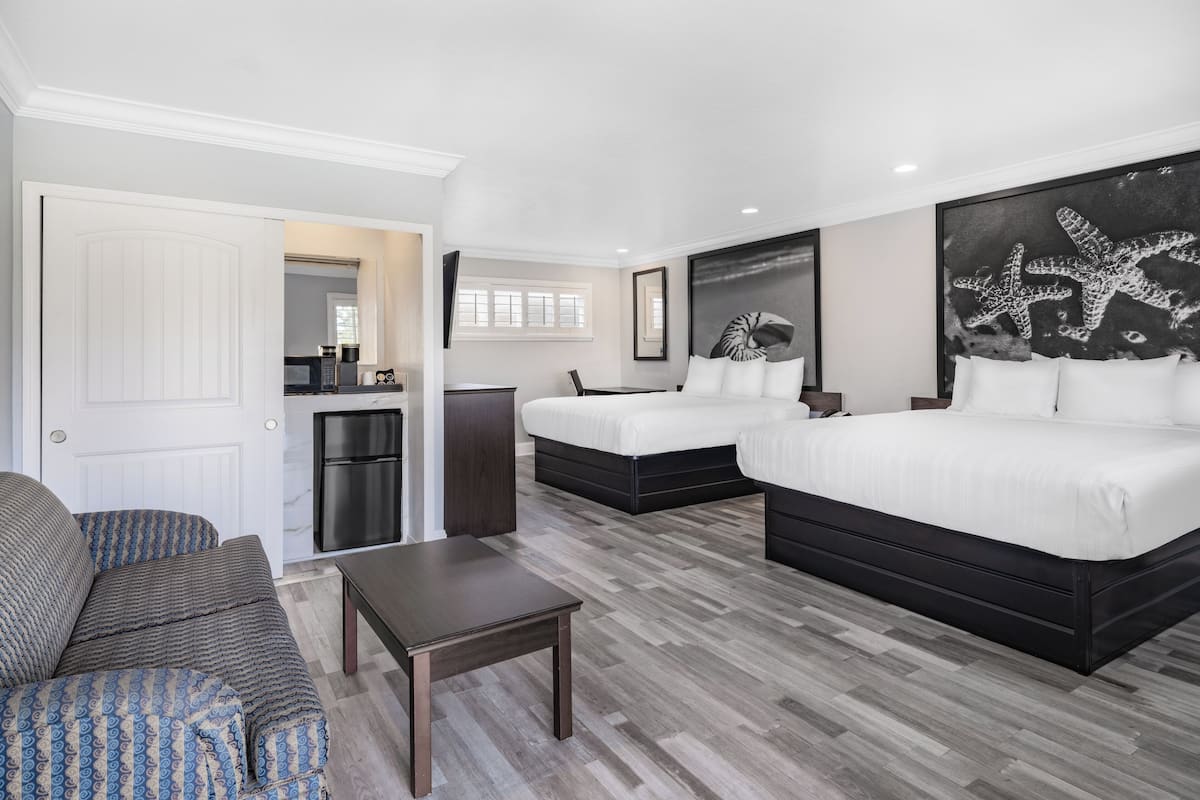A hotel room with two beds, a sofa, a coffee table, and artwork on the walls.