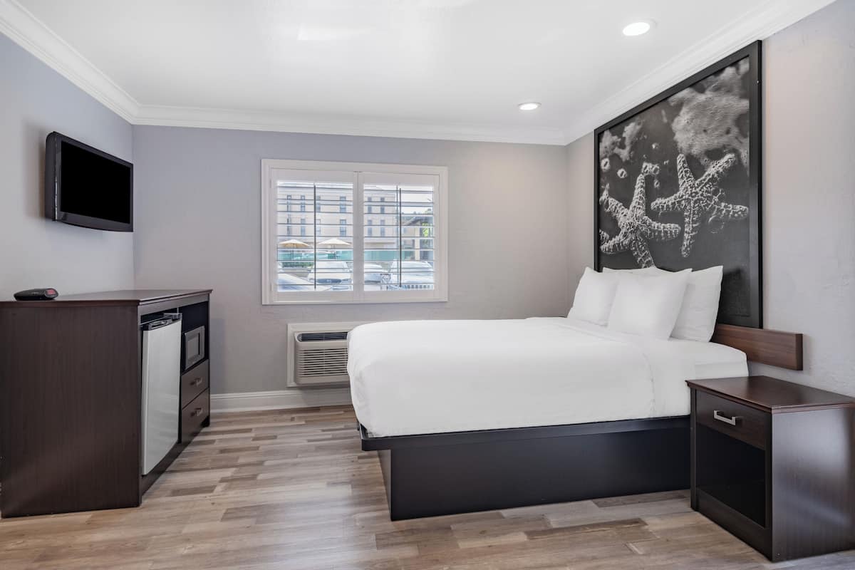 A modern hotel room with a large bed, a flat-screen TV, a desk, and a window with a view of the city.