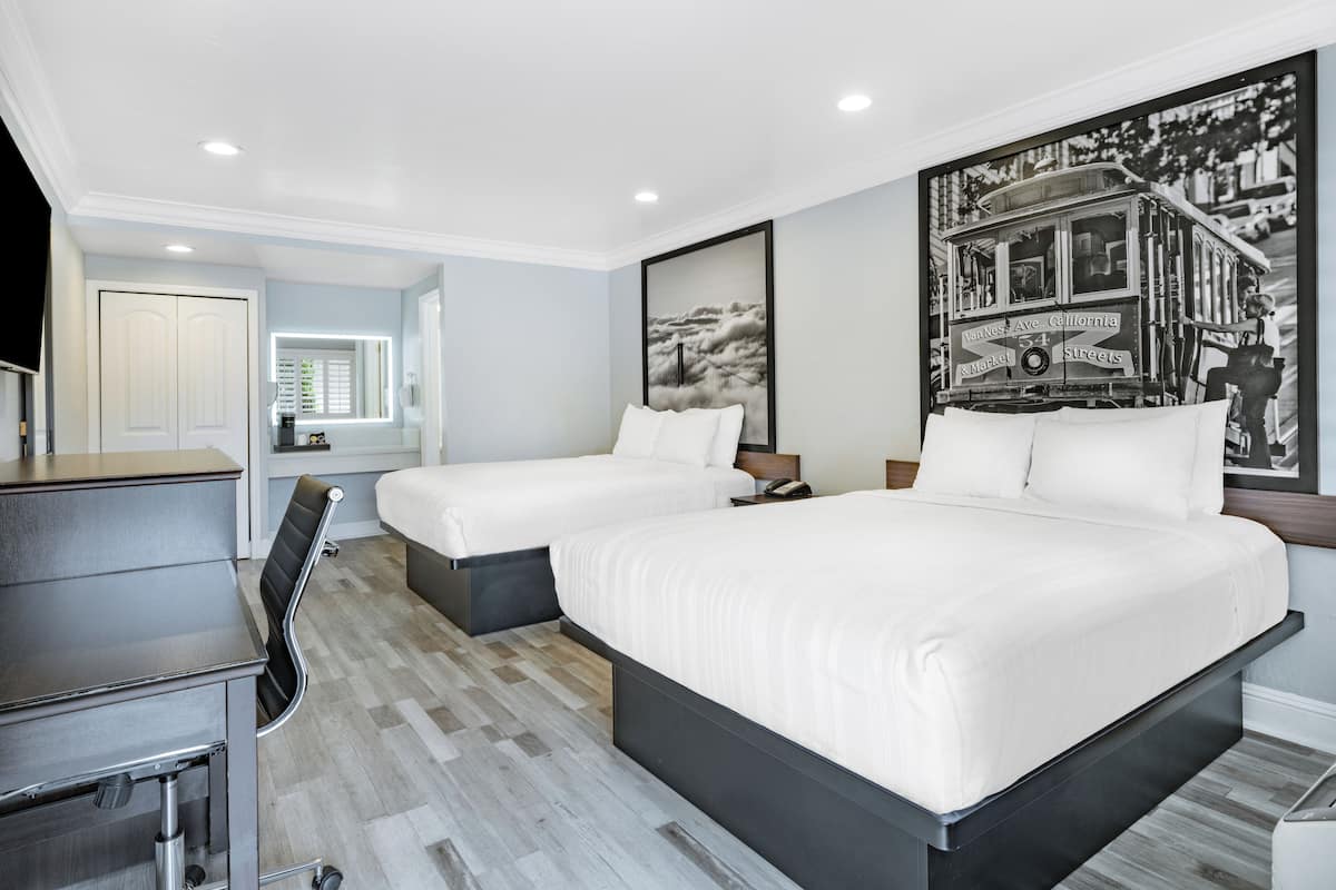 A hotel room with two beds, a desk, and a large framed picture of a trolley on the wall.