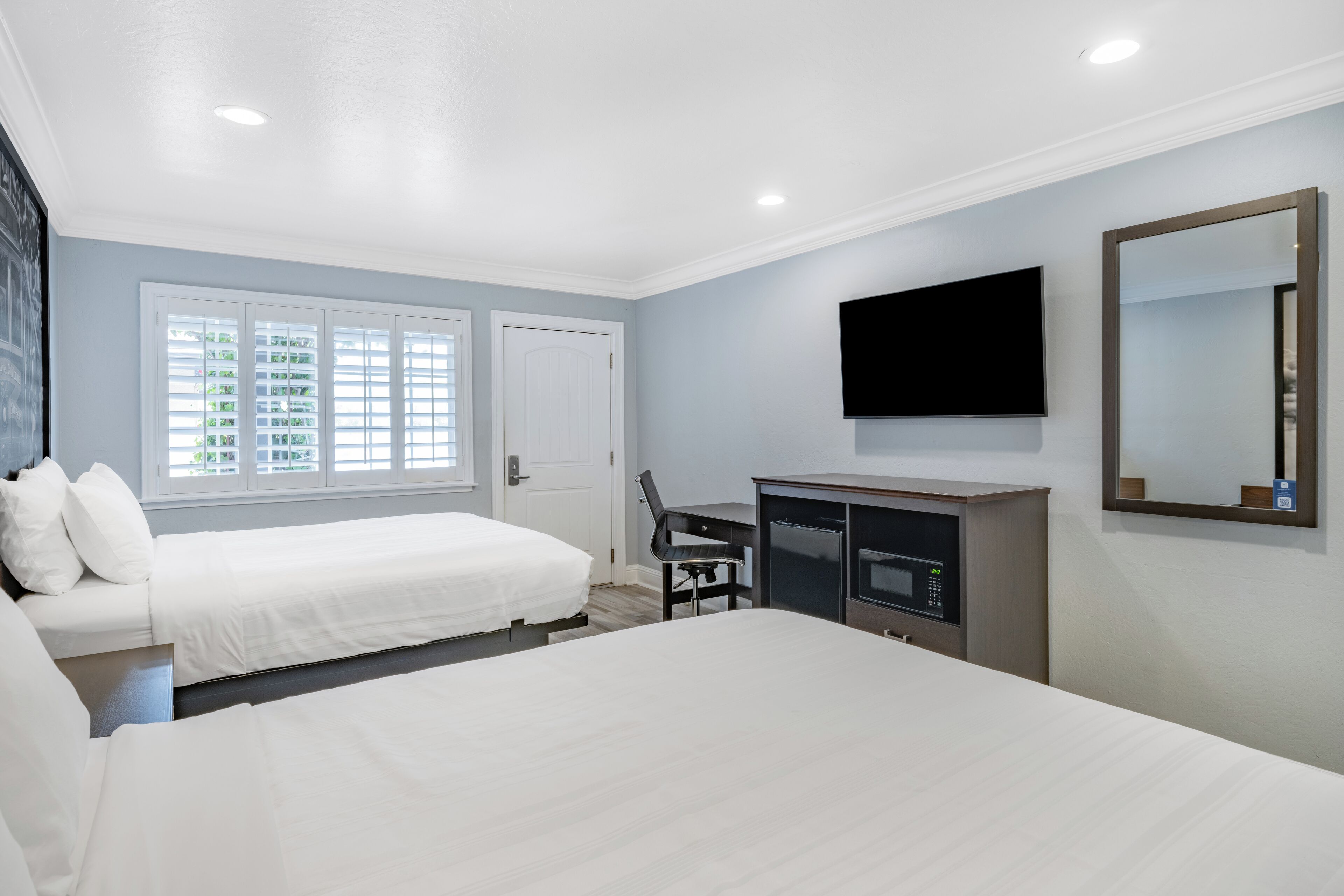 A hotel room with two beds, a desk with a microwave, a TV, and a large mirror.