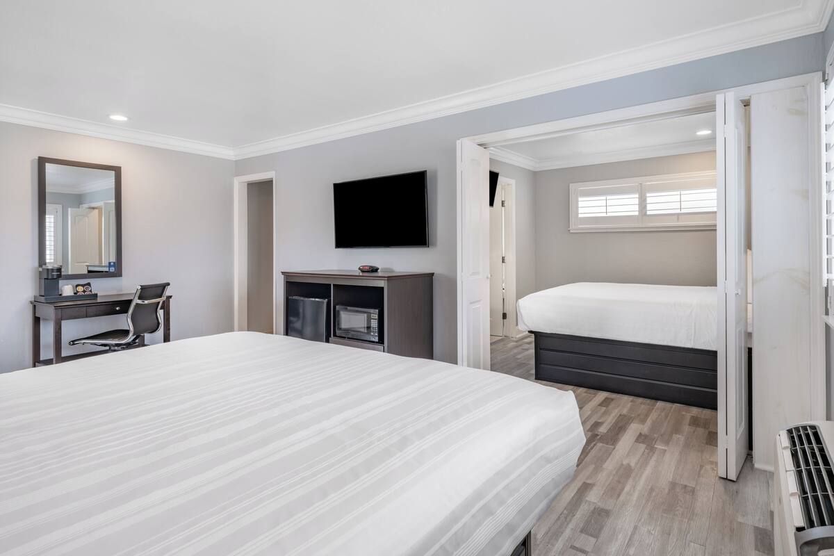 A modern hotel room with a large bed, a desk with a chair, a flat-screen TV, a microwave, and a window with blinds.