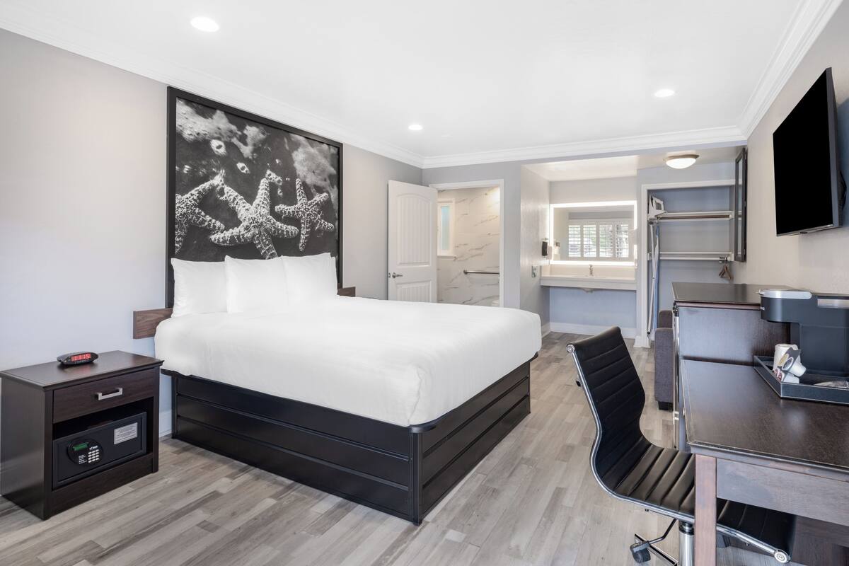 A modern hotel room with a large bed, a desk, a chair, a TV, and a bathroom visible through an open door.