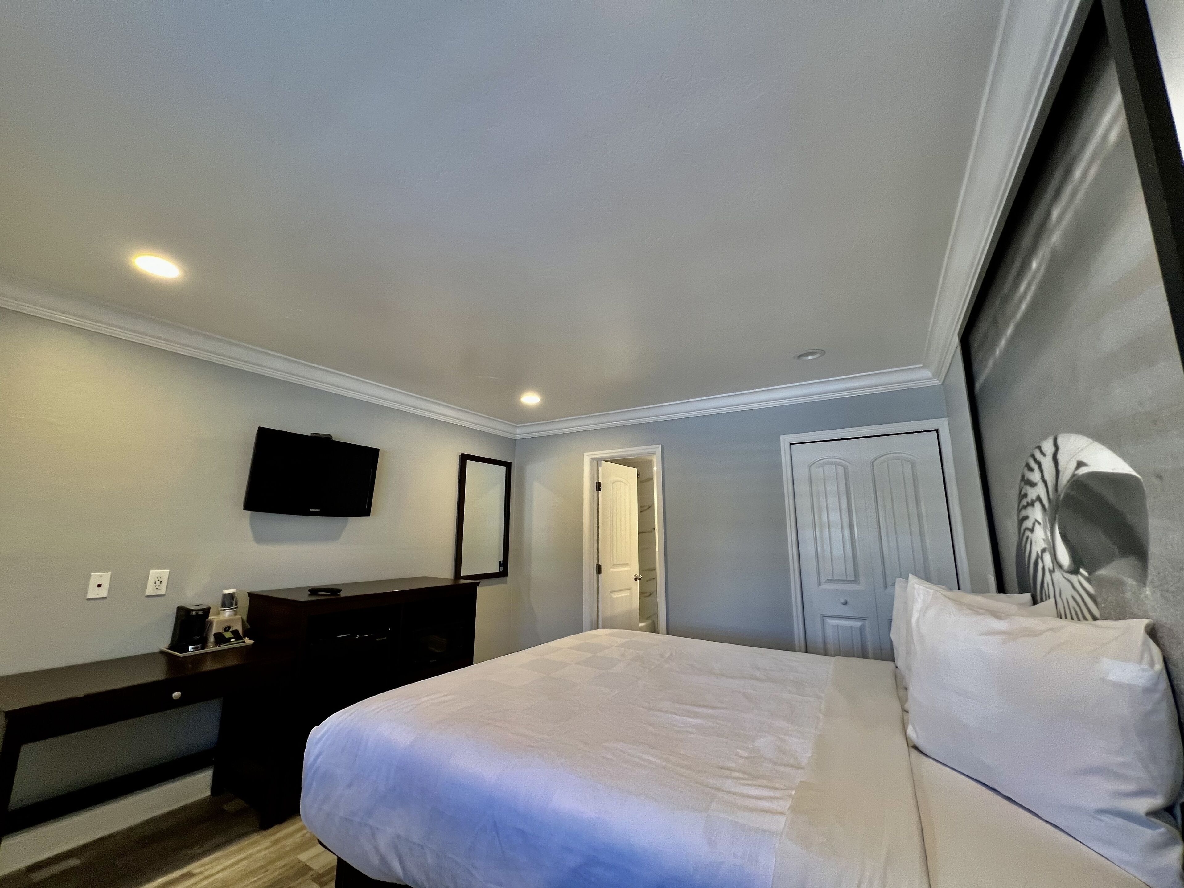 A bedroom with a bed, a TV mounted on the wall, a dresser, and a door leading to another room.