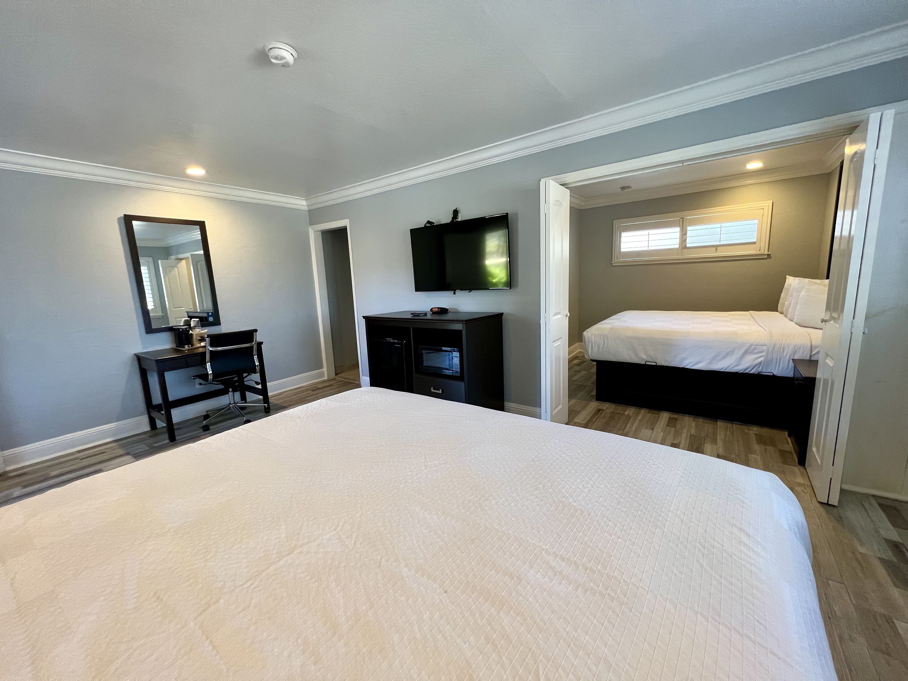 A bedroom with a large bed, a desk with a chair, a TV, and a window.
