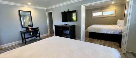 A bedroom with a large bed, a desk with a chair, a TV, and a window.