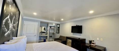 A hotel room with a large bed, a desk, a television, and a bathroom visible through an open door.
