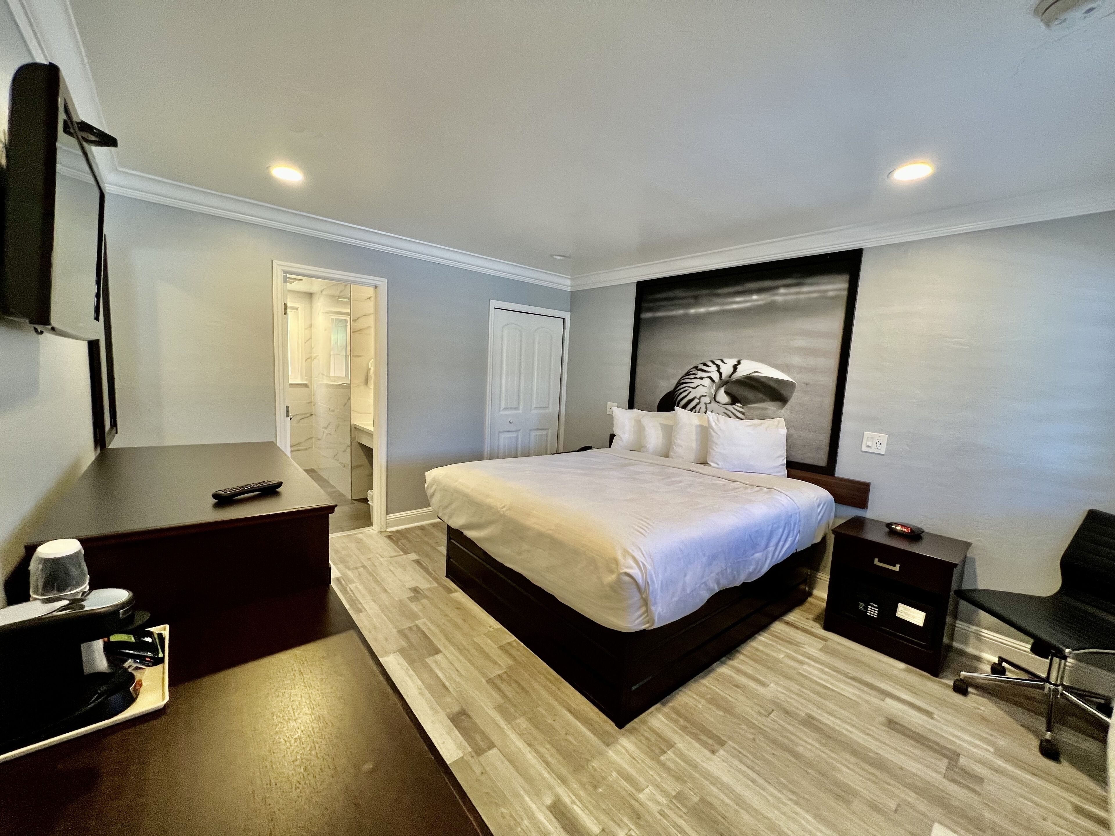 A modern hotel room with a large bed, a desk, a chair, and a flat-screen TV.