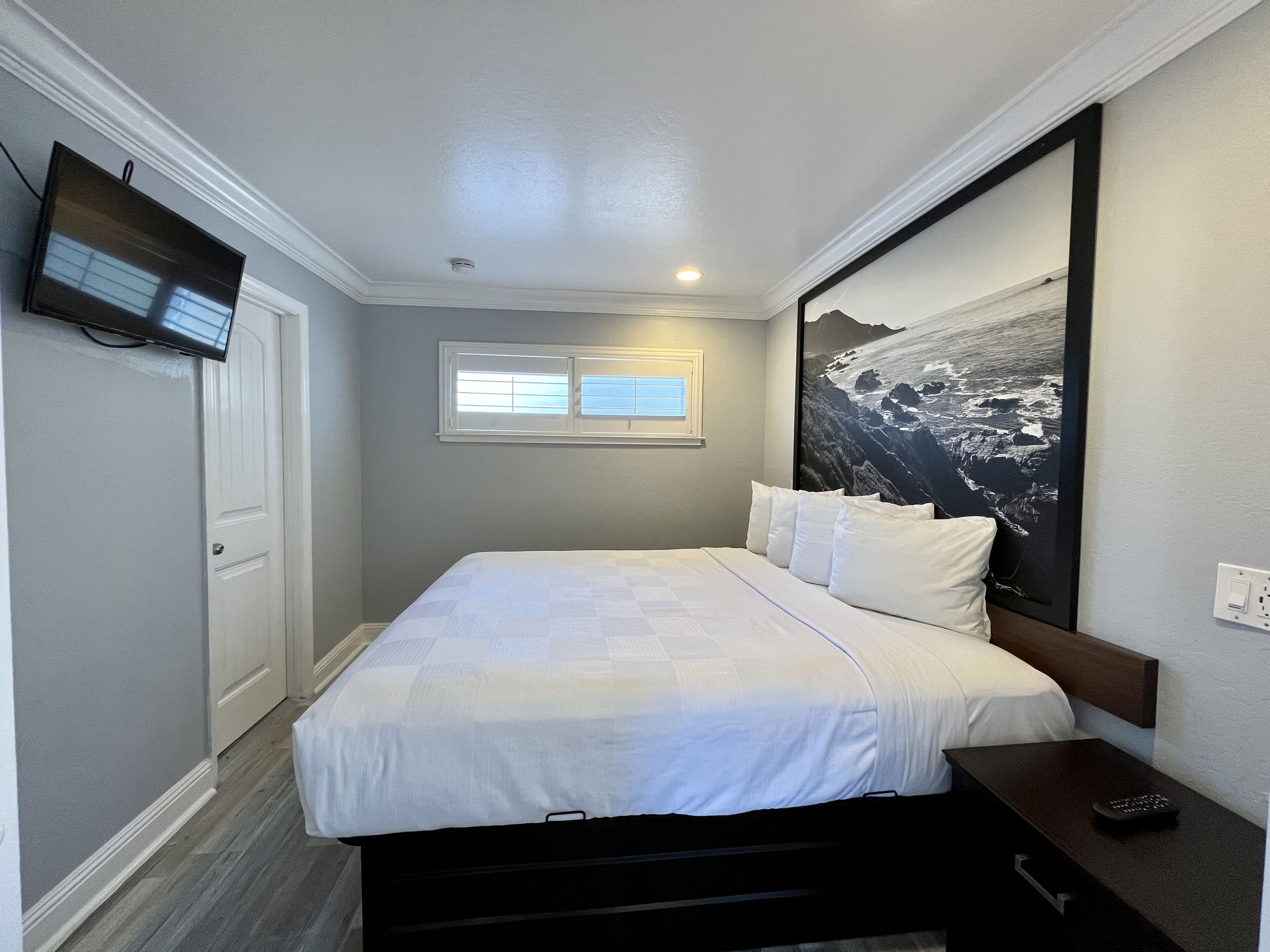 Une chambre à coucher avec un lit, un téléviseur fixé au mur, une fenêtre et un tableau.