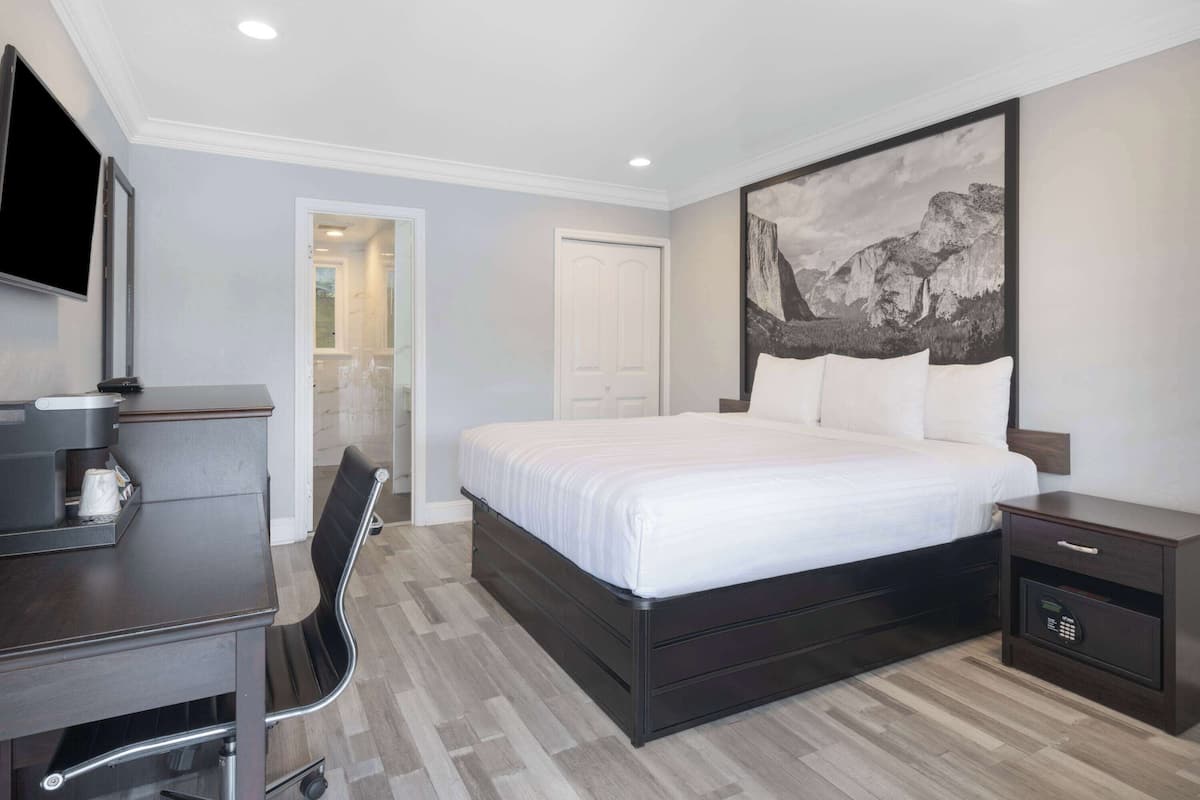 A modern hotel room with a large bed, a desk with a coffee maker, a chair, and a nightstand with a phone.