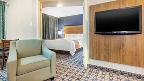 A hotel room with a bed, a TV, a sofa, and a patterned carpet. - Quality Suites Whitby (Whitby)